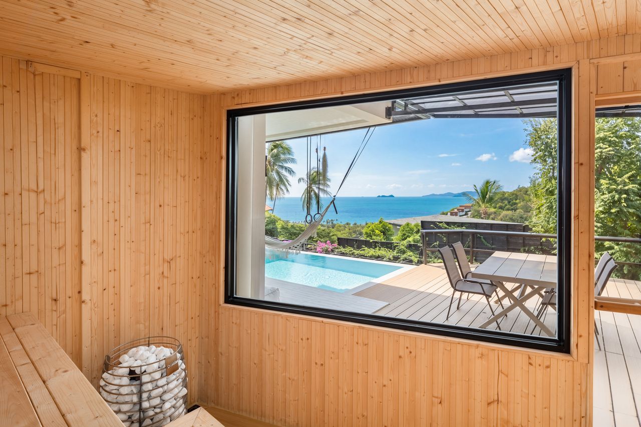 Inside the wooden sauna, a large window looks out over the pool and sea